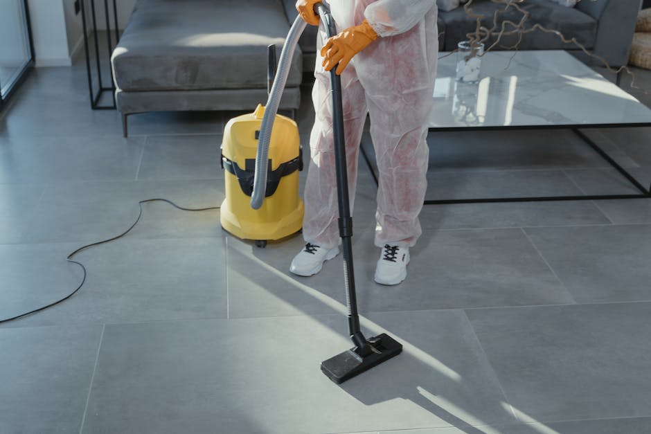 A clean, empty room with light-colored wooden flooring and beige walls illuminated by natural light from a window. In the corner, there is a wooden window frame and a white radiator below the window. On the floor, there is a yellow-handled cleaning brush and a wooden window sash removal tool resting nearby, indicating ongoing window surface cleaning or replacement. The scene reflects thorough preparation and surface cleaning, consistent with professional domestic cleaning services by Cleaners SW7, related to avoiding common end of tenancy cleaning mistakes in Kensington, SW7, focusing on detailed surface and window maintenance.